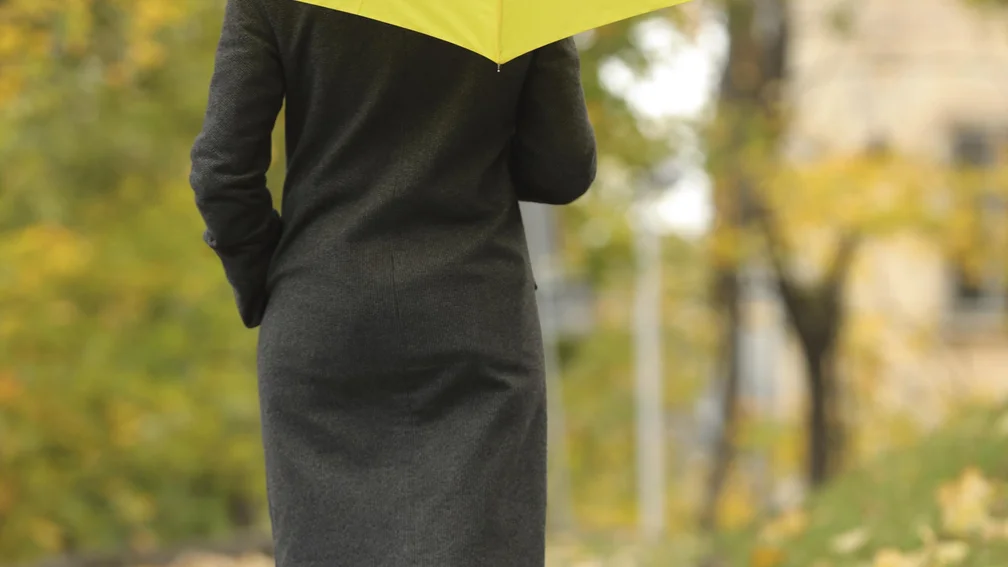Person von hinten mit gelbem Regenschirm und gelben Gummistiefeln