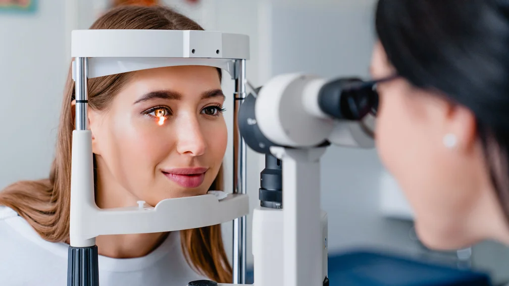 junge Frau bei einer Untersuchung beim Augenarzt; Augenärztin leuchtet der Patientin mit einem Untersuchungsgerät in das Auge
