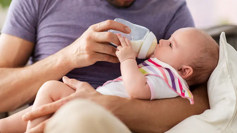 Vater hält Säugling im Arm und gibt ihm die Flasche