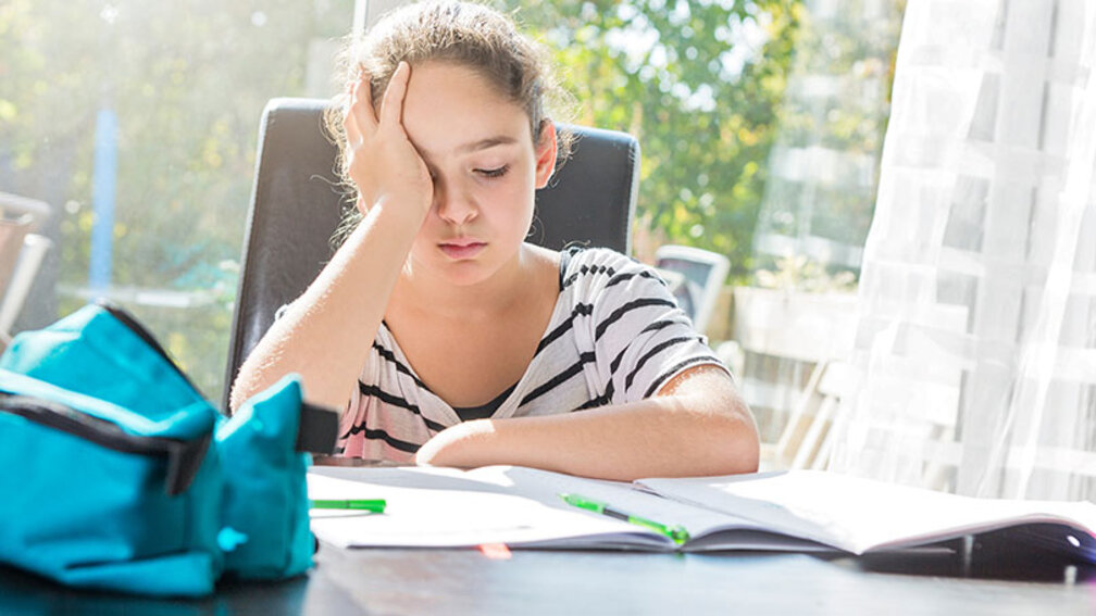 Schulmädchen sitzt erschöpft vor Hausaufgaben