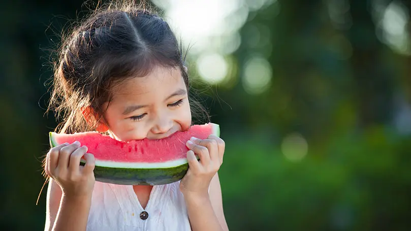dunkelhaariges Mädchen beißt in eine große Scheibe Wassermelone