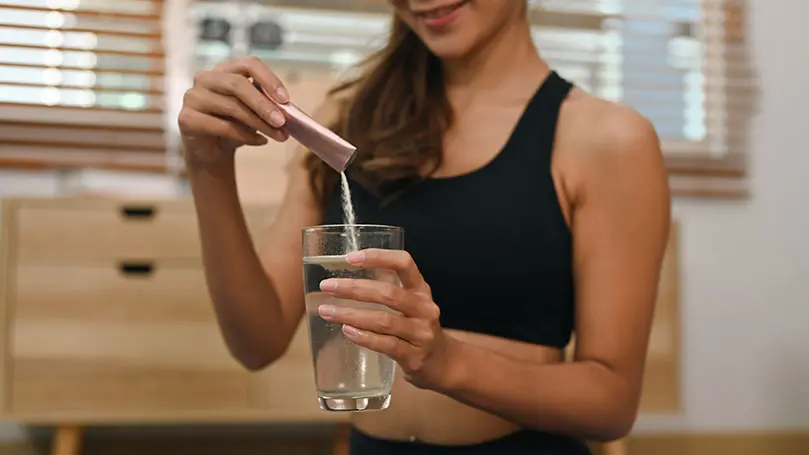 Junge Frau in Sportkleidung schüttet ein Trinkpulver in ein mit Wasser gefülltes Glas