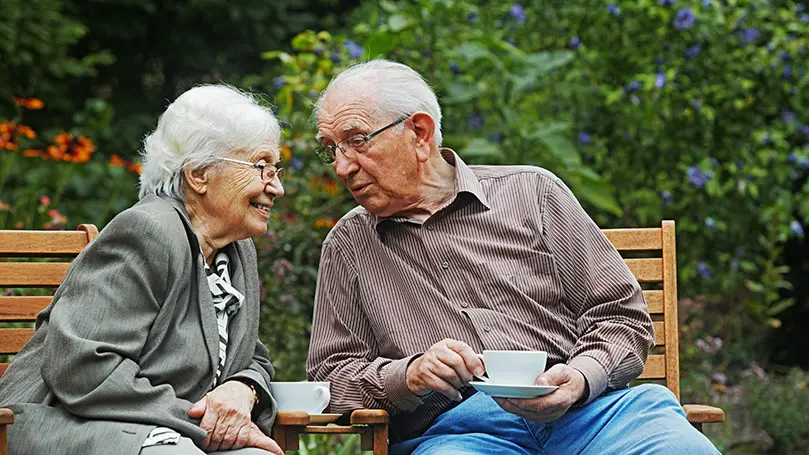 Ein älteres Paar sitzt auf Gartenstühlen und trinkt Kaffee