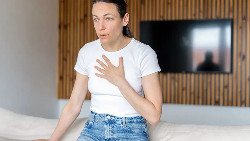 Frau mittleren Alters sitzt schwer atmend auf einem Sofa