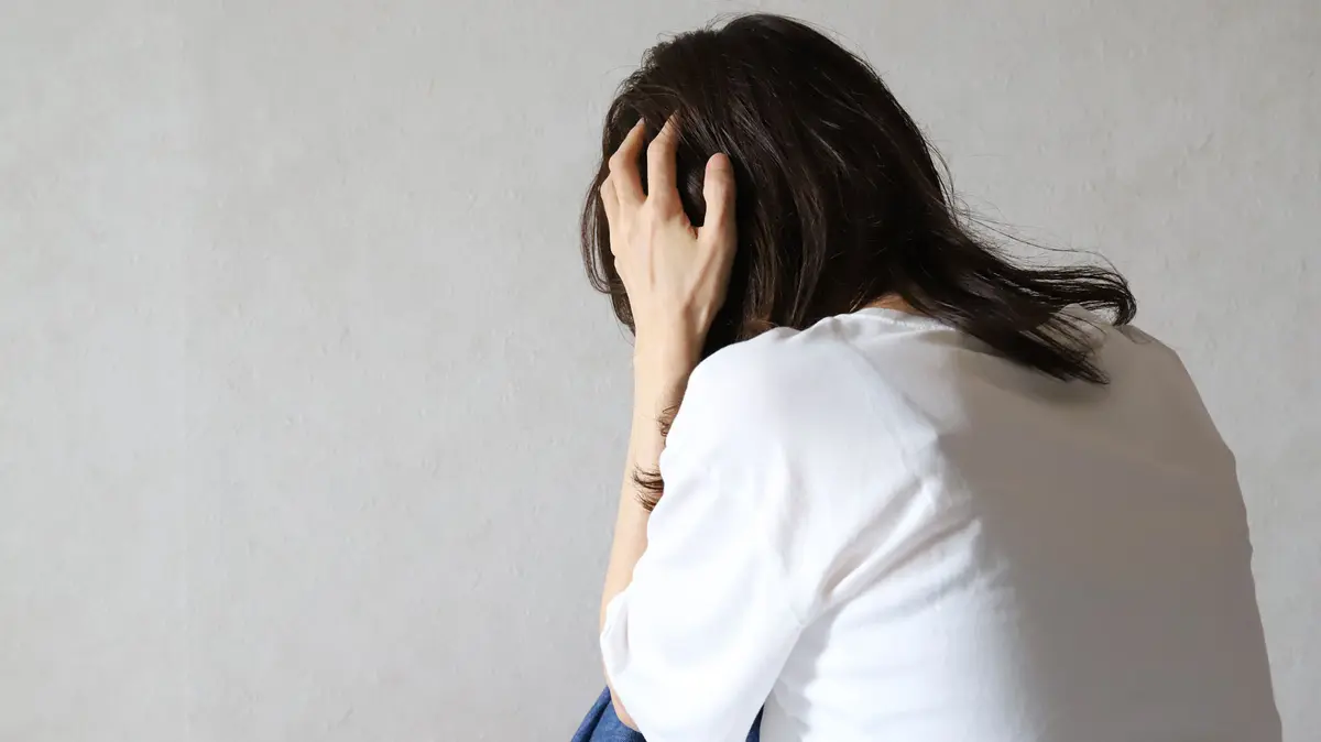 Frau sitzt mit dem Rücken zugewandt auf dem Boden und hält mit den Händen seitlich den Kopf