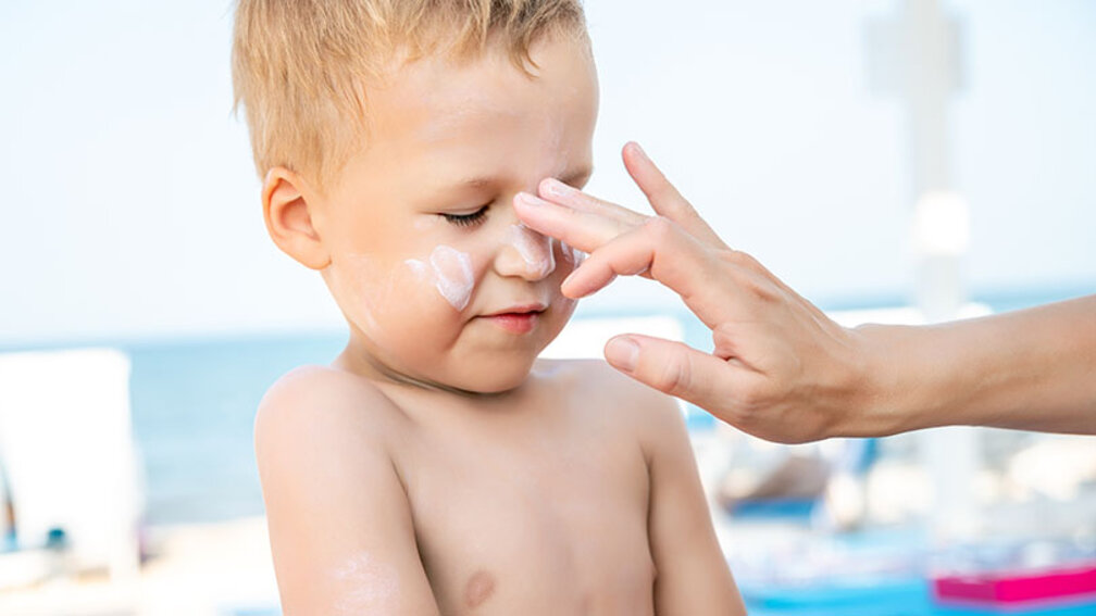 Mutter cremt Jungengesicht mit Sonnencreme ein
