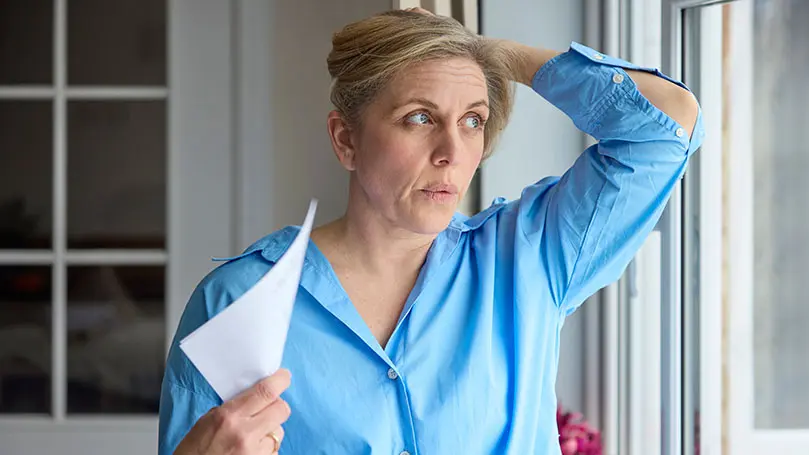 Frau mittleren Alters in blauem Hemd, hält sich Haare aus dem Nacken und fächert sich mit Blatt Papier Luft zu