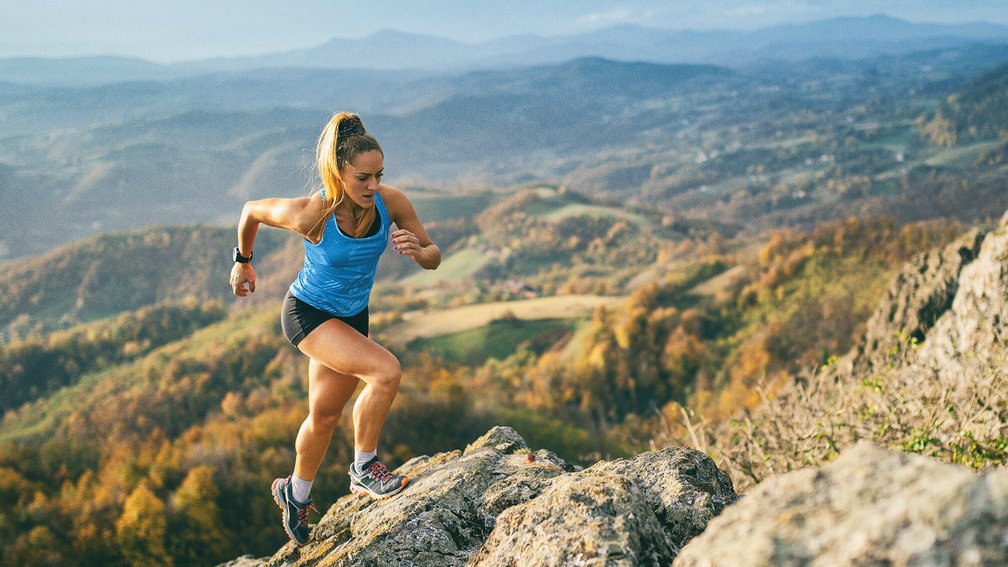 Blonde trainierte Frau joggt Felsen hoch