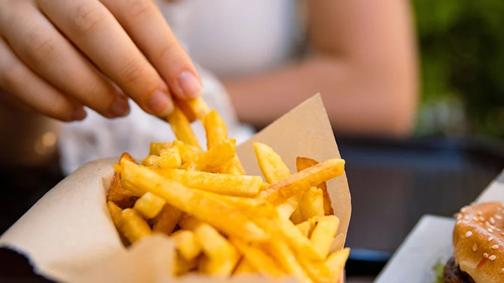 Junge Frau greift mit drei Fingern nach Pommes