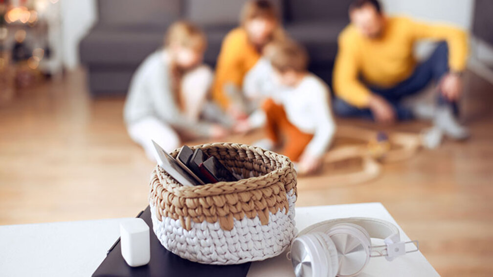 In einem Korb auf einem Tisch liegen drei ausgeschaltete Smartphones