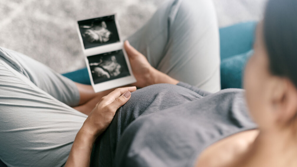 schwangere Frau fasst sich an den Bauch und schaut ein Ultraschallbild an