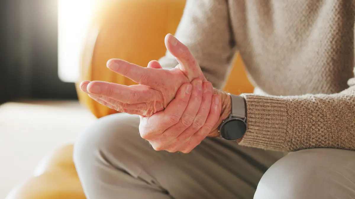 Mann fasst sich mit der rechten Hand an die andere Hand und spreizt dabei die Finger