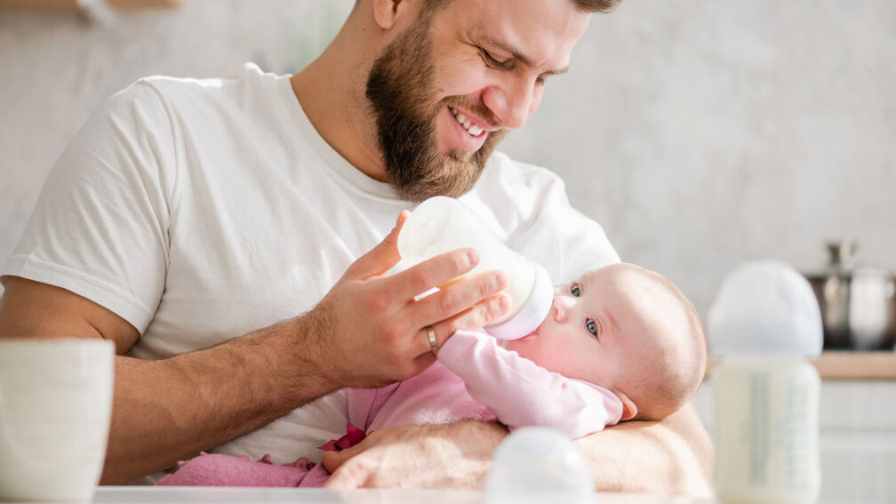 Vater hält Baby in dem Arm und füttert es mit einem Fläschchen