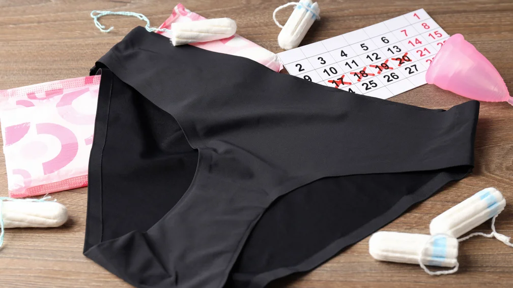 schwarzer Slip, Tampons, Menstruationstasse und Slipeinlagen liegen auf einer Ablage