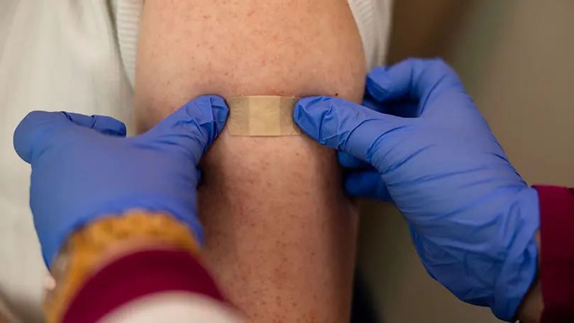 zwei Hände in blauen Gummihandschuhen kleben Pflaster auf einen Oberarm