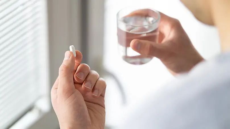 Mann im weißen Shirt hält Tablette in der einen und ein gefülltes Wasserglas in der anderen Hand