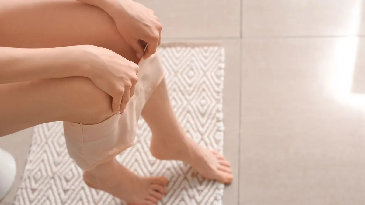 Frau mit beige farbenem Slip sitzt auf der Toilette