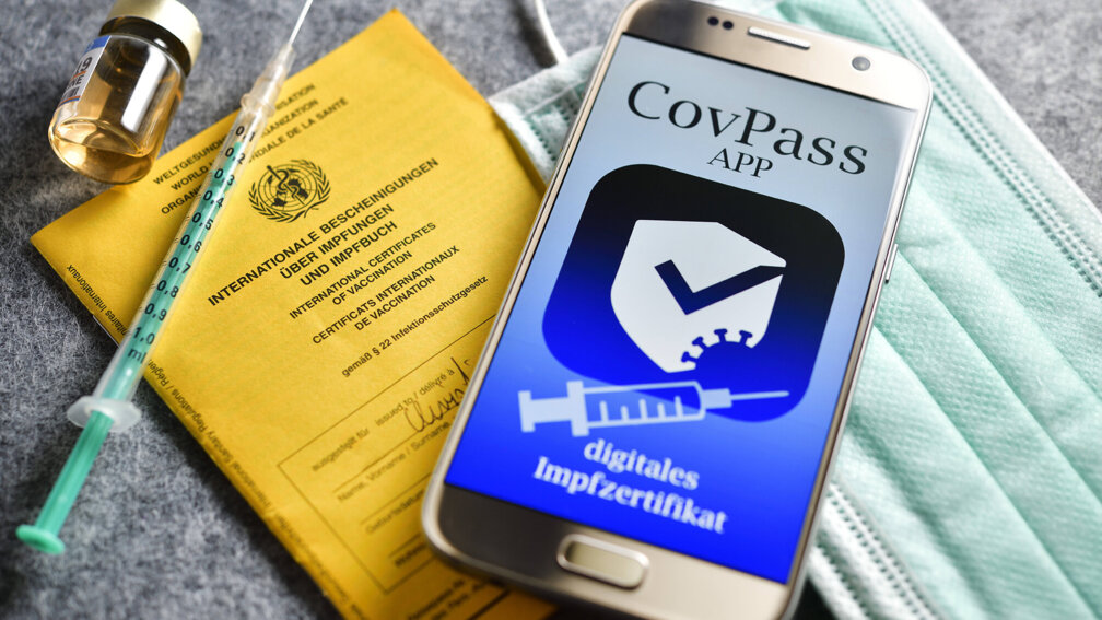 Impfbuch, Maske, Injektionsspritze, Handy mit CovPass auf grauem Untergrund