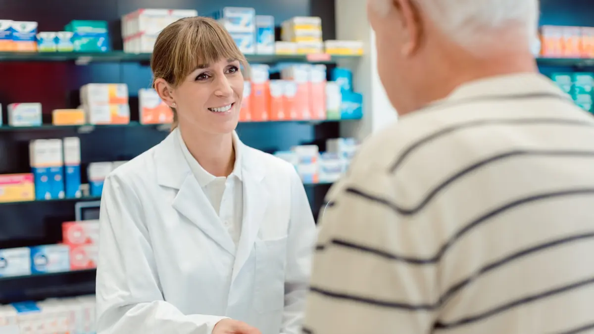 Junge, lächelnde Apothekerin überreicht älterem Herrn etwas