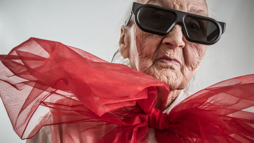 Seniorin mit Sonnenbrille und großer roten Schleife um den Hals