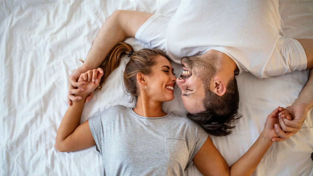 Frau und Mann liegen Kopf an Kopf im Bett und lachen