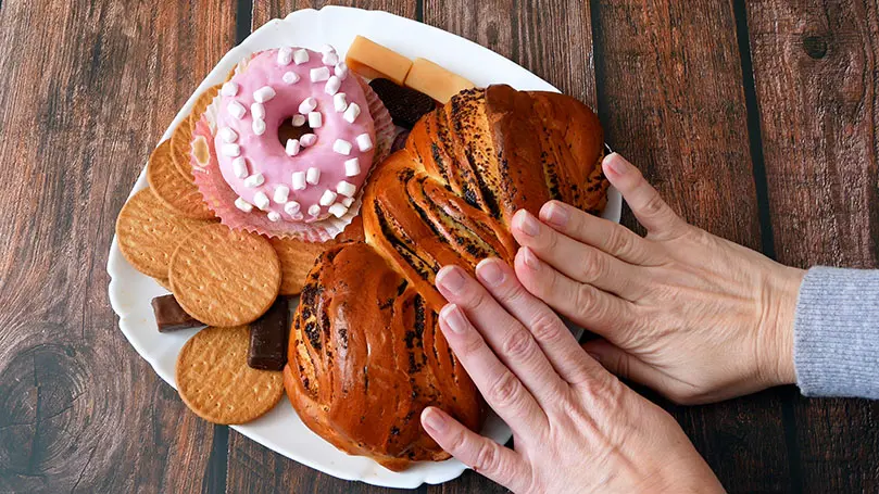 zwei Frauenhände schieben Teller mit Süßigkeiten weg