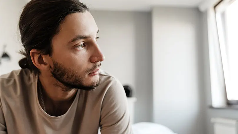 junger Mann mit dunklen Haaren blickt deprimiert zur Seite