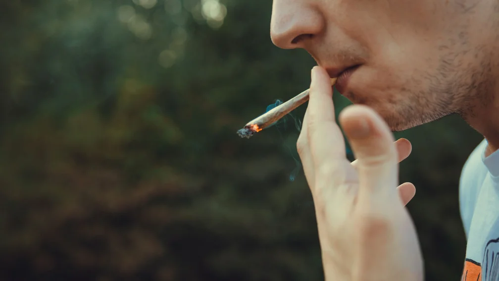 Jugendlicher hält einen Joint in der Hand und zieht daran