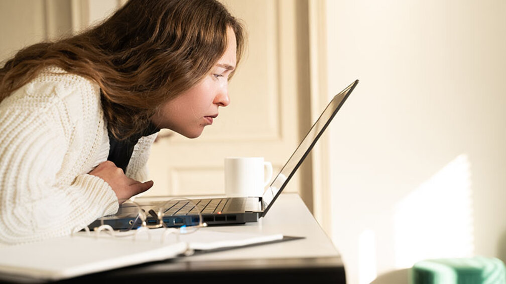 Junge Frau kann schlecht sehen und lehnt dicht über dem Laptop