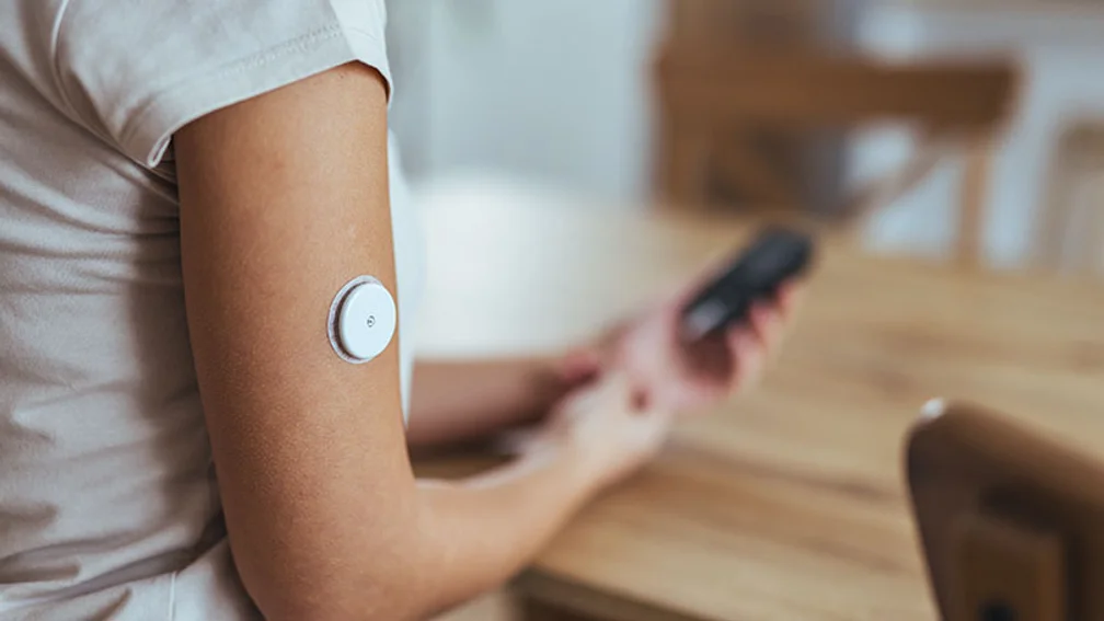 Frau mit Glukosemessungs-Patch am Oberarm schaut auf ihr Handy