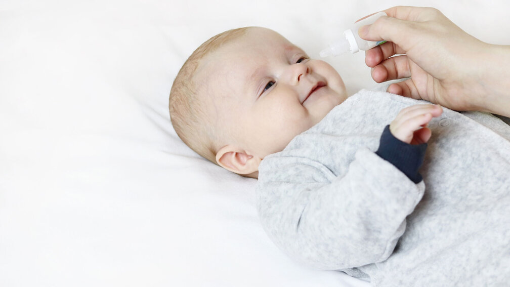 Baby liegt auf dem Rücken, Nasentropfen werden verabreicht